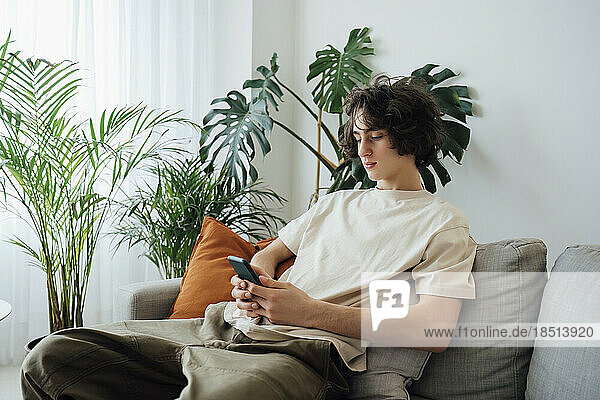 Teenage boy using smart phone sitting on sofa at home