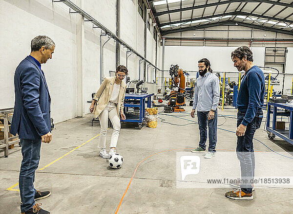 Business colleagues playing with soccer ball in factory