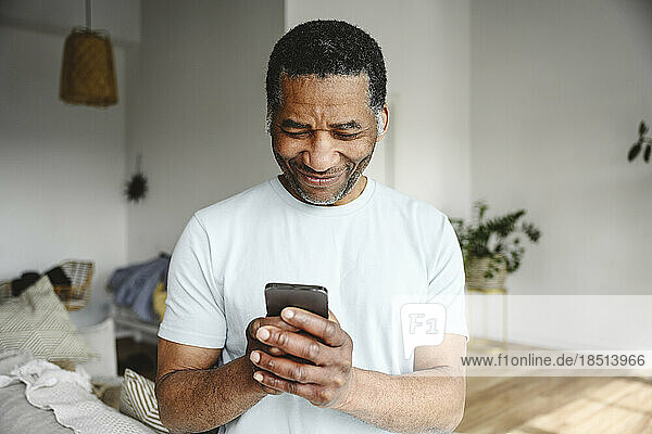 Smiling mature man using mobile phone in living room at home