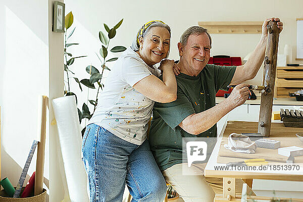 Happy senior woman with hand on shoulder on man applying varnish to wood in workshop