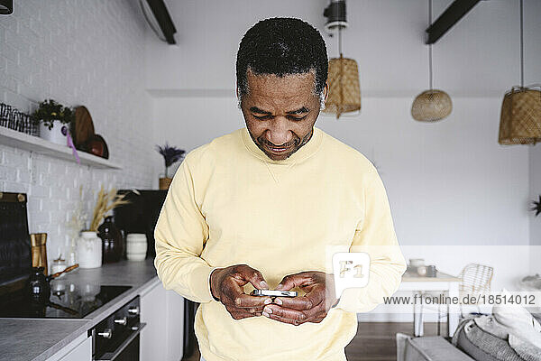 Mature man using smart phone in kitchen at home