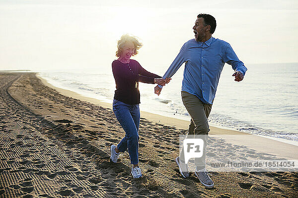 Cheerful mature woman running with man at coastline