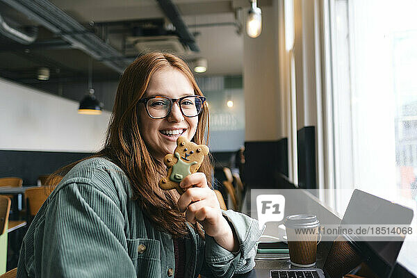 Happy young freelancer with teddy bear cookie in cafe