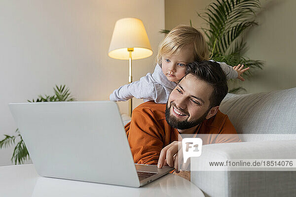 Happy father using laptop with son lying on father at home