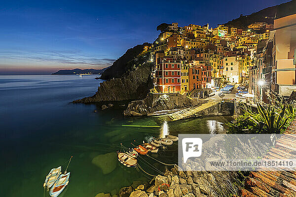 Italy  Liguria  Riomaggiore  Boats moored at edge of coastal village along Cinque Terre at dusk
