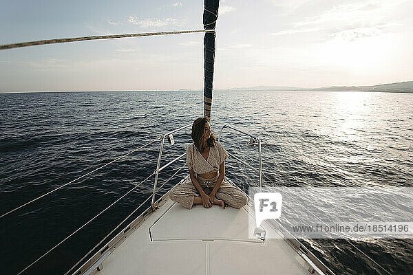 Woman sitting on sailboat and enjoying vacation at sunset