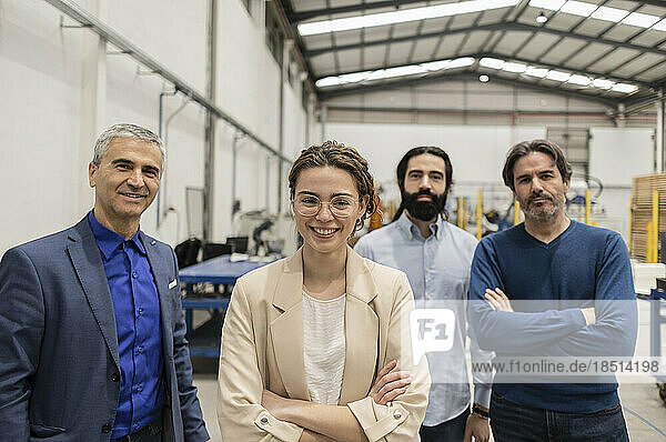 Happy young engineer standing with colleagues at factory