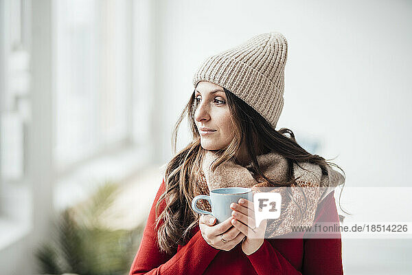 Contemplative woman wearing knit hat having coffee at home