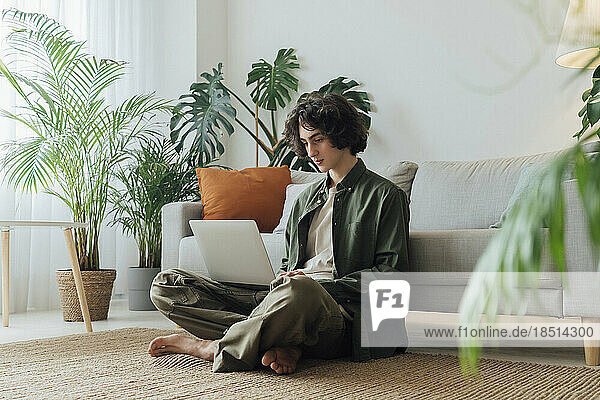Freelancer using laptop sitting on carpet in front of sofa at home