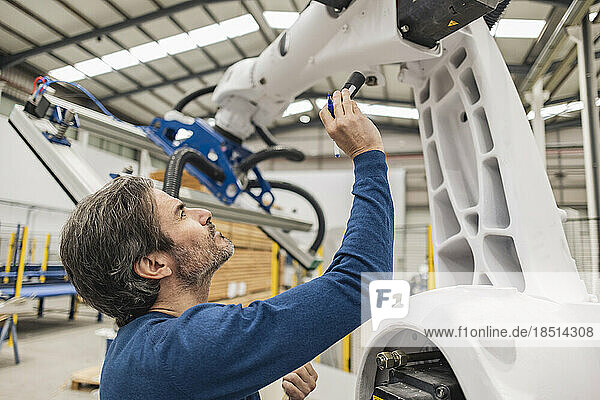 Engineer examining robotic arm with flashlight in industry
