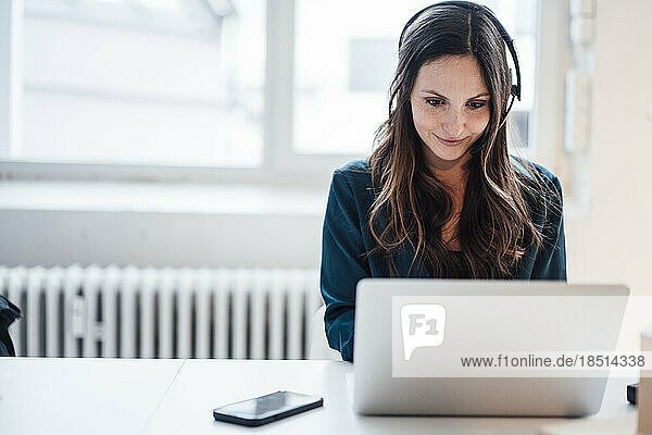 Young businesswoman wearing headphones working on laptop at home office
