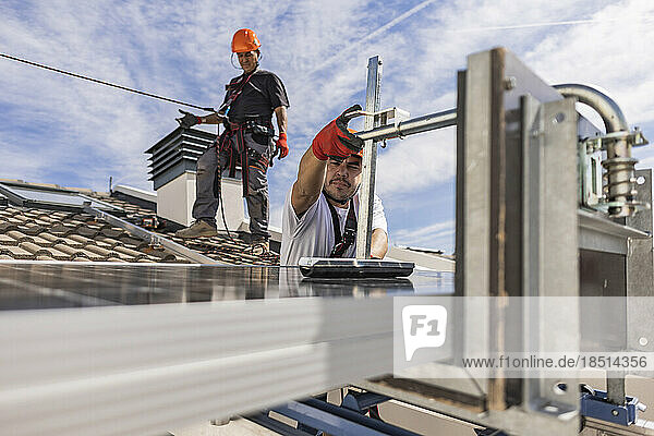 Engineers installing solar panel on roof under sky
