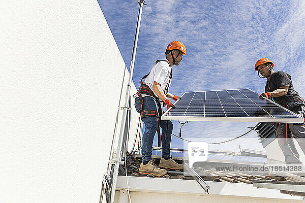Young technician with colleague installing solar panels on roof