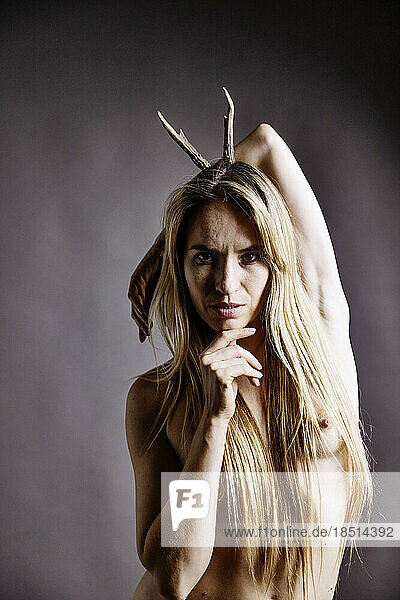 Naked woman with deer horned on head against colored background