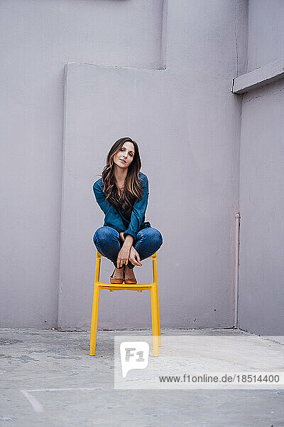 Young woman sitting on yellow chair in front of wall