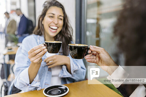 Cheerful friends toasting coffee cup and enjoying at sidewalk cafe