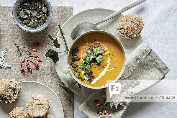 Studio shot of bowl of pumpkin soup with homemade buns in Christmas setting
