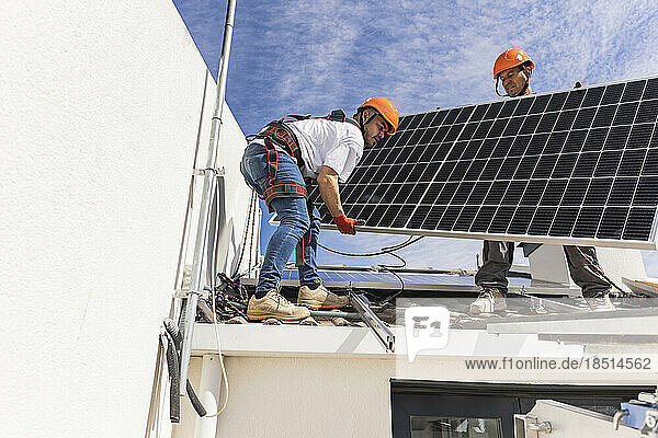 Technician with colleague installing solar panel on roof