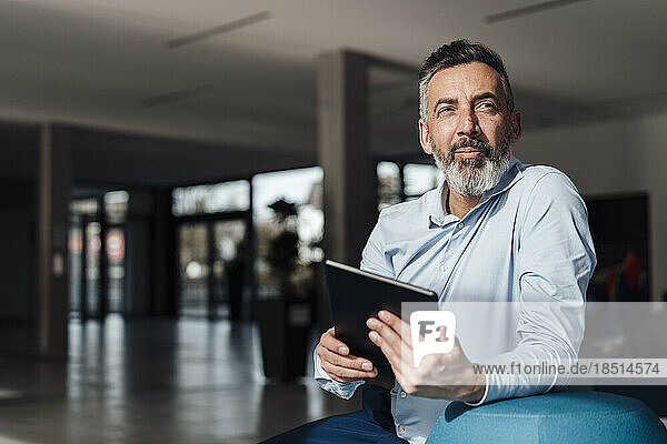 Thoughtful mature businessman sitting with tablet PC in office