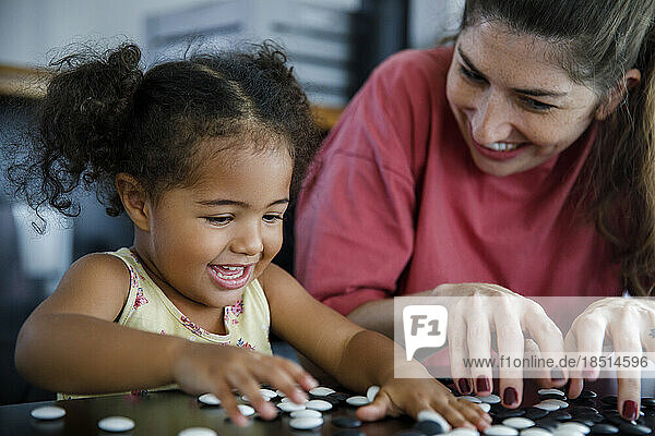 Happy mother and daughter playing go game at home