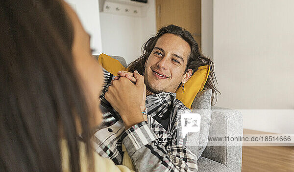 Smiling man holding girlfriend's hand lying on sofa in apartment