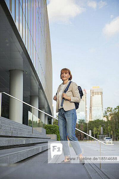 Mature businesswoman with backpack standing on steps