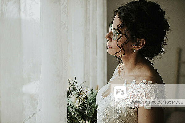 Nachdenkliche Braut mit Blumenstrauß  die aus dem Fenster schaut