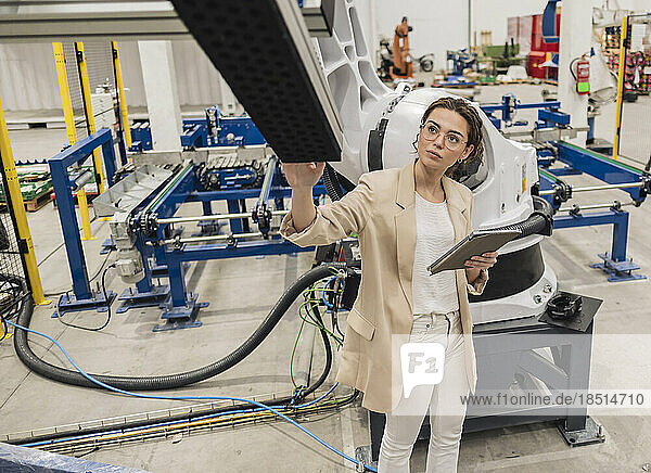 Young engineer wearing eyeglasses examining robotic arm