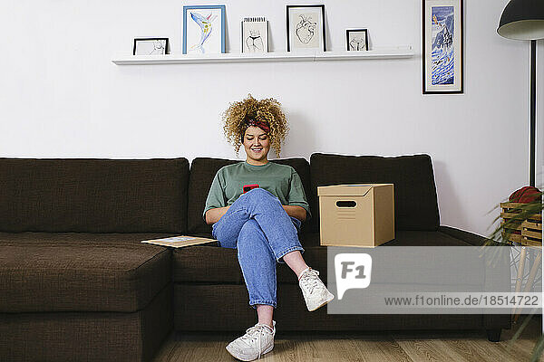 Smiling young woman using smart phone on sofa at home