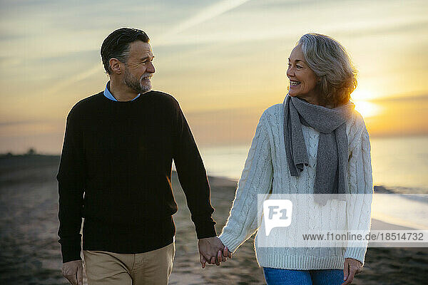 happy mature couple holding hands and walking at beach