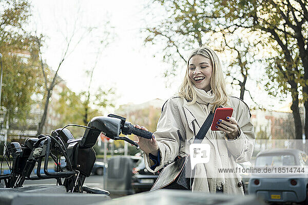Glückliche Frau mit Smartphone steht am Fahrradparkplatz