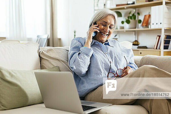 Glückliche ältere Frau  die zu Hause über ihr Mobiltelefon telefoniert
