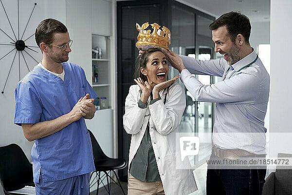 Happy doctor giving crown to colleague in clinic