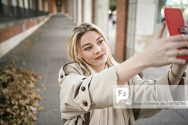 Woman taking selfie through smart phone on footpath