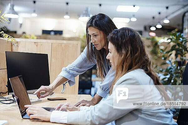 Businesswoman with colleague discussing over laptop in office