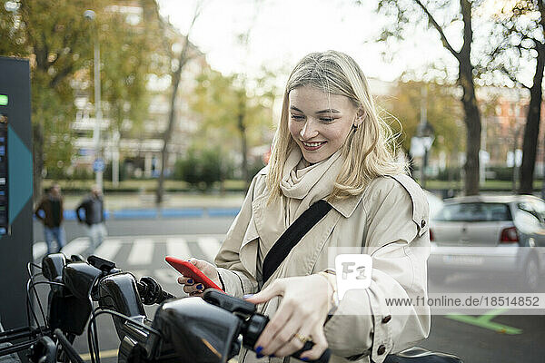 Smiling woman renting electric bicycle at parking station