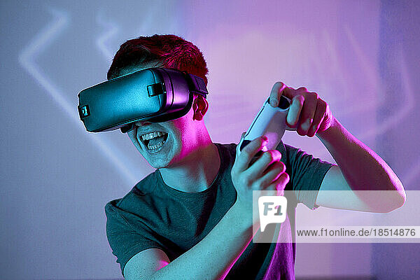 Young man wearing VR glasses playing video game in front of wall