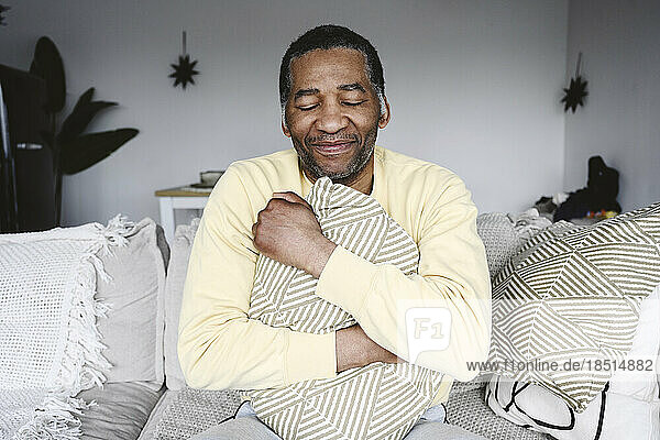 Smiling mature man hugging pillow sitting on sofa at home