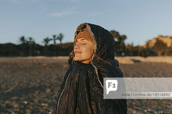 Smiling woman with eyes closed in sleeping bag at beach