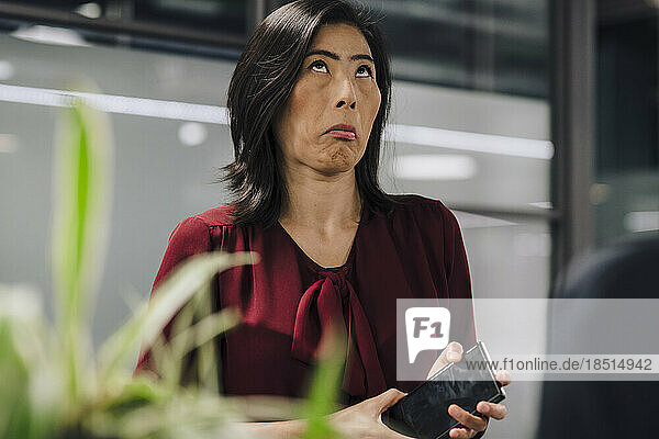 Businesswoman making a face holding smart phone at office