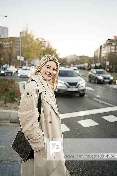 Smiling young woman with hand in pocket standing on street