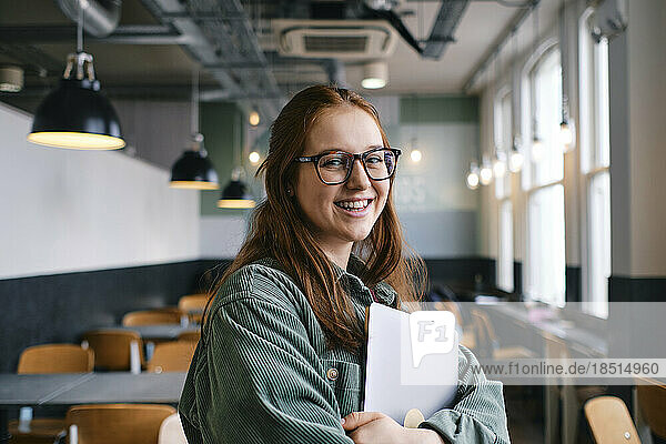Smiling young freelancer standing with laptop in cafe