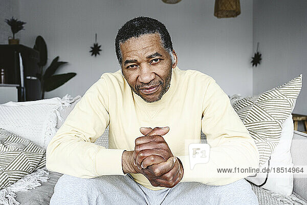 Mature man with hands clasped sitting on sofa at home