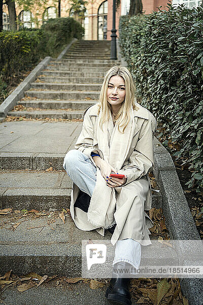 Young woman with smart phone sitting on steps in autumn