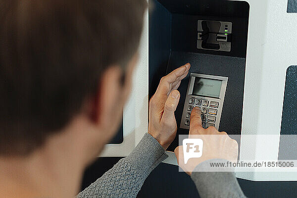 Mann gibt PIN in Geldautomaten ein