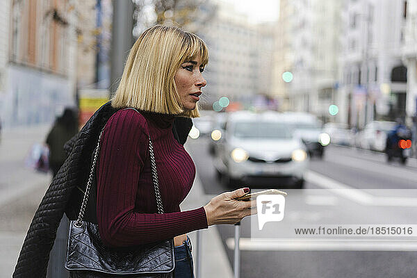 Woman holding smart phone waiting on sidewalk