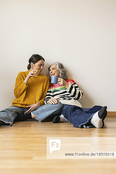 Happy mother and daughter with coffee cup sitting on floor