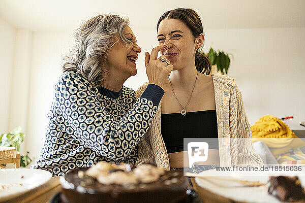 Happy mother applying chocolate on nose of daughter at home