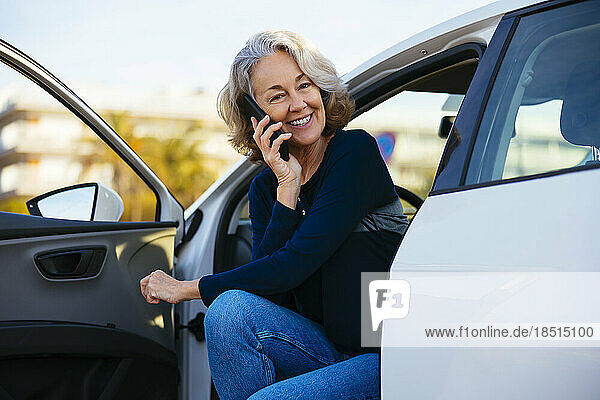 Glückliche reife Frau  die im Auto mit dem Smartphone spricht