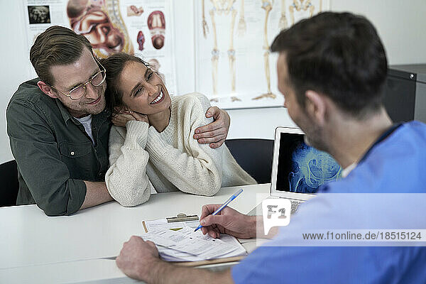 Glückliches Paar mit Arzt  der in der Klinik über ein Rezept diskutiert